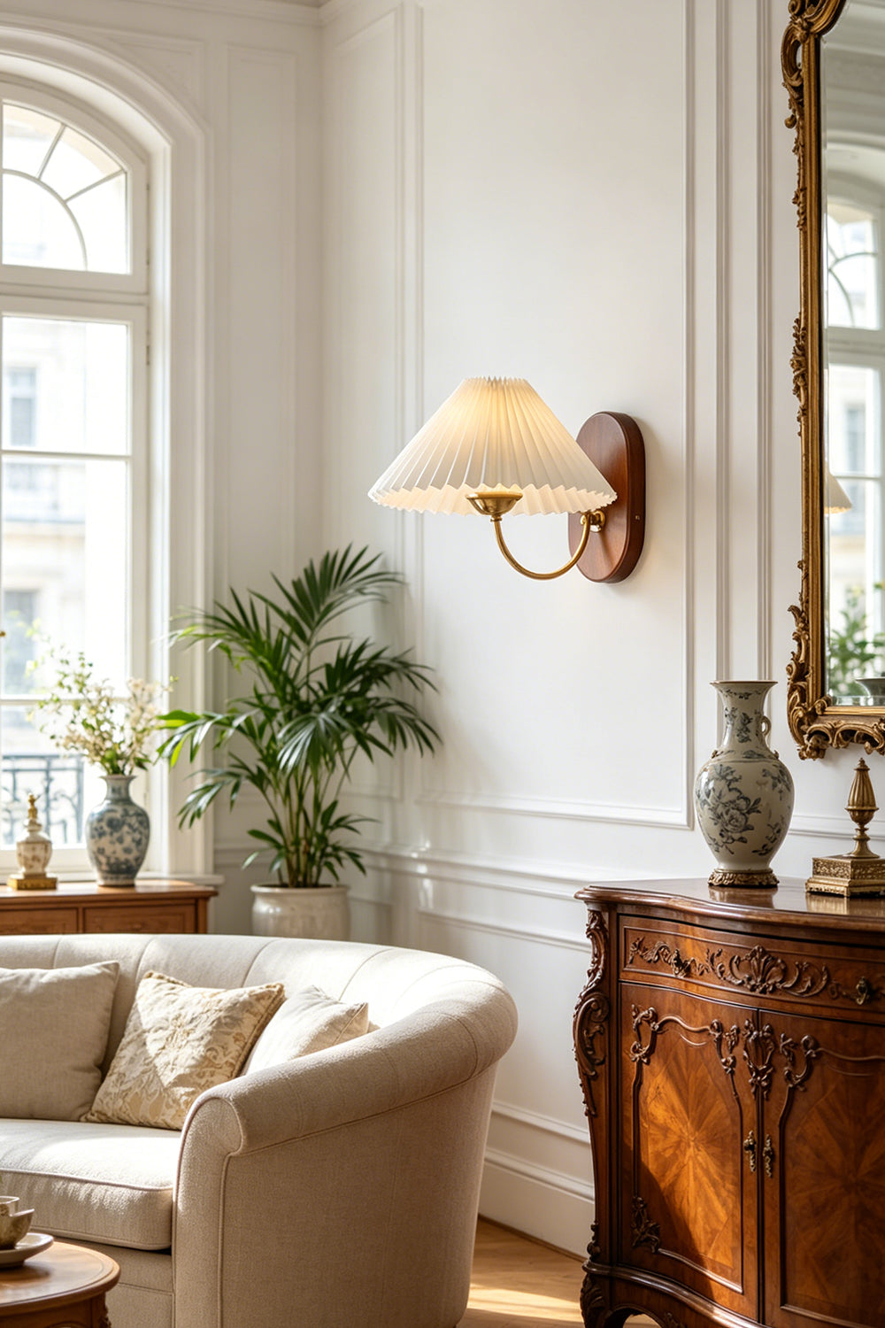 Pleated Fabric Wall Lamp | Fabric, Metal, Wood | Mounted on a wall as accent lighting in a classic living room with a tufted cream sofa and a large arched window | vexa lamps