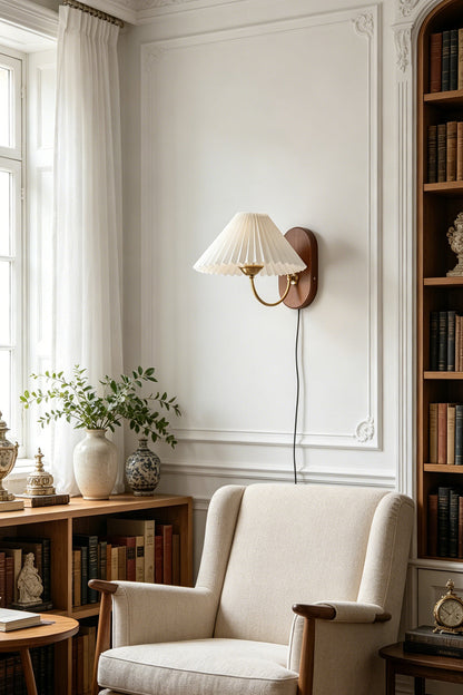 Pleated Fabric Wall Lamp | Fabric, Metal, Wood | Providing a cozy warm glow over a fabric armchair in a bright reading corner next to a wooden bookshelf | vexa lamps
