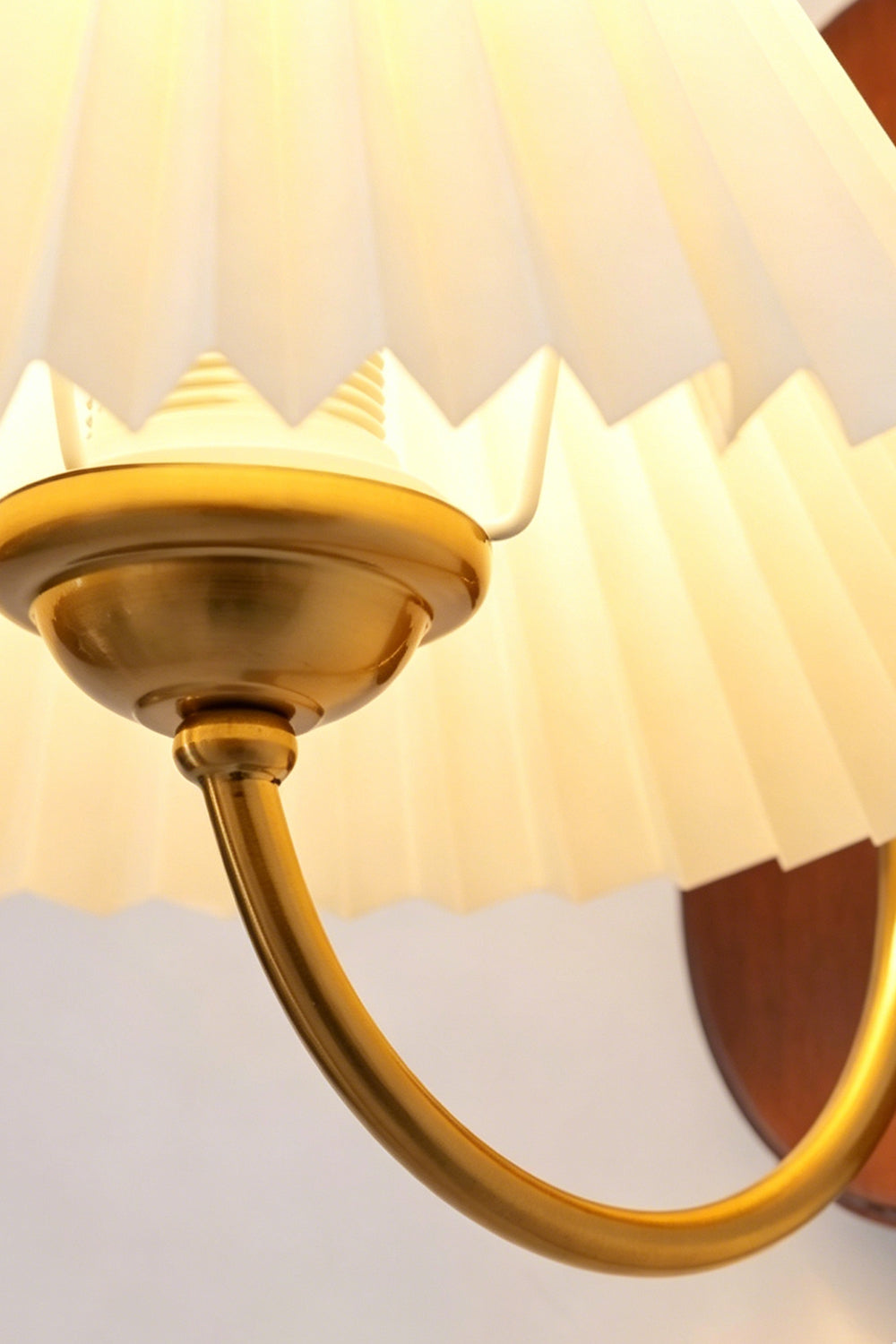 Pleated Fabric Wall Lamp | Fabric, Metal, Wood | Close-up view from underneath focusing on the curved brass support arm and light socket attachment | Detail shot | vexa lamps