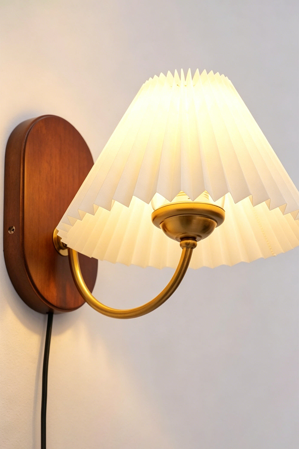 Pleated Fabric Wall Lamp | Fabric, Metal, Wood | Side angle profile view of the illuminated pleated lamp radiating soft ambient light on a plain wall with a visible black cord | vexa lamps