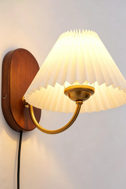 Pleated Fabric Wall Lamp | Fabric, Metal, Wood | Side angle profile view of the illuminated pleated lamp radiating soft ambient light on a plain wall with a visible black cord | vexa lamps