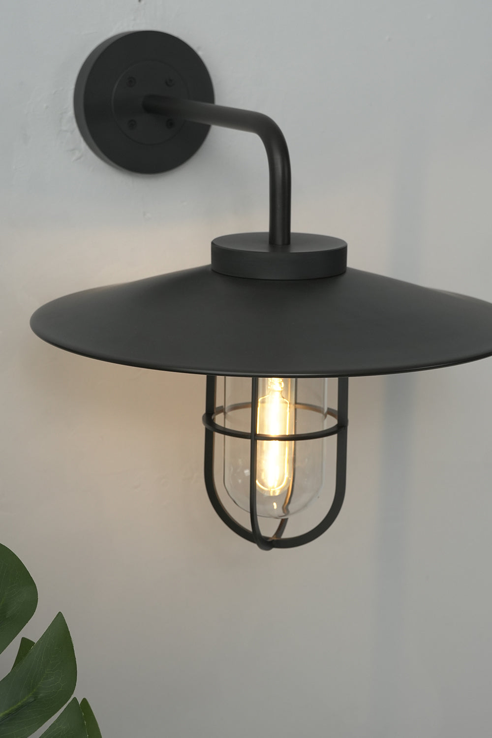 Lit black Portree wall light in studio setting | Metal, Glass | Close-up showing warm bulb glow | vexa lamps