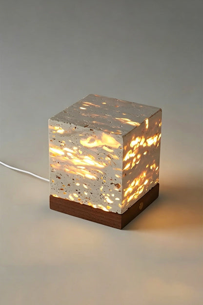 Radiant Monolith Travertine Table Lamp | Travertine, Wood | Lit front view on plain background | Intricate internal light pattern | Dark wood base, gold button | vexa lamps