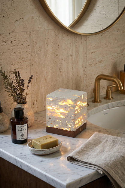 Radiant Monolith Travertine Table Lamp | Travertine, Wood | Unlit on marble vanity | Spa-like bathroom corner | Round mirror, toiletries, towels | vexa lamps