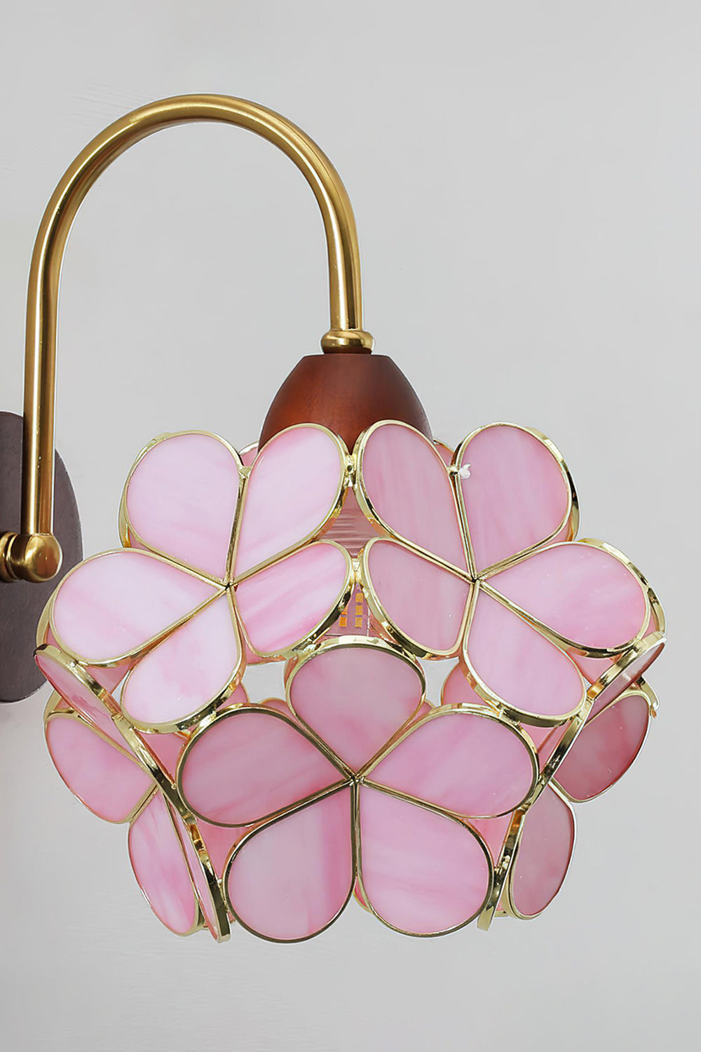Rosalind Petal Glass Botanical Wall Lamp | Glass, Metal, Wood | Side angled view of the lit pink flower petal wall light casting a soft pinkish-gold halo on a plain studio wall | vexa lamps