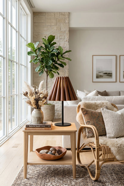 Rowan Leather Pleated Table Lamp | Leather, Metal | Placed on a light oak side table next to a woven armchair and a large window in a bright living room | vexa lamps
