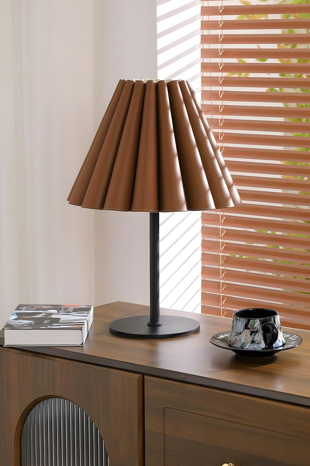 Rowan Leather Pleated Table Lamp | Leather, Metal | Situated on a sleek dark wood sideboard cabinet near window blinds in a contemporary workspace | vexa lamps