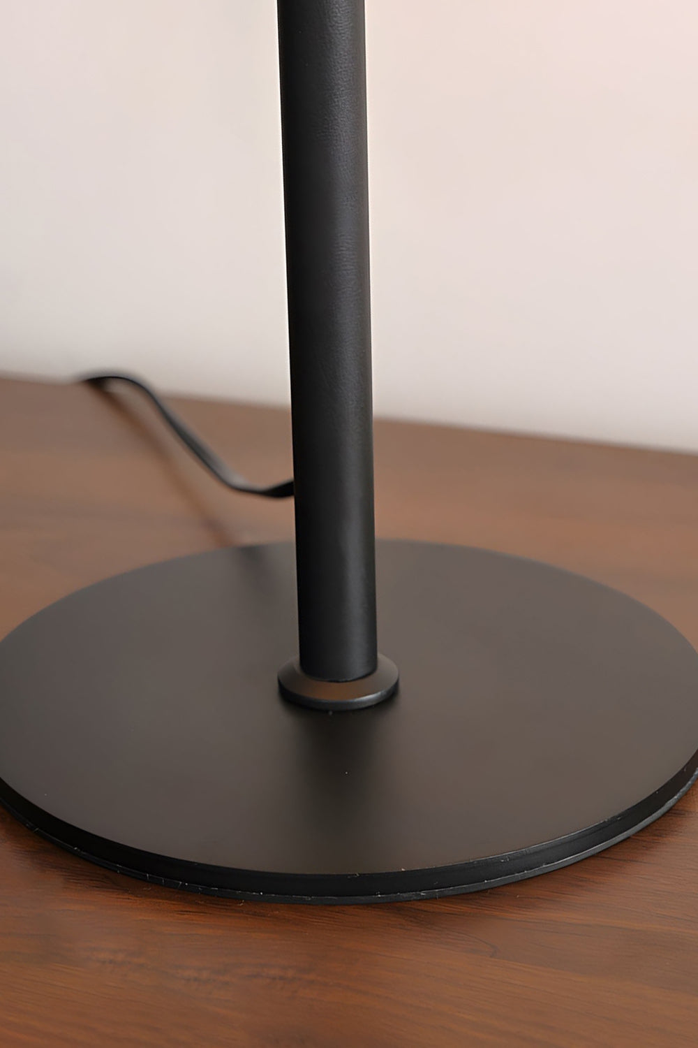 Rowan Leather Pleated Table Lamp | Leather, Metal | Close-up focus on the flat circular matte black metal base plate resting on a polished wooden surface | Detail shot | vexa lamps