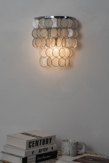 Lit Shimmering Round Capiz Wall Lamp | Shell | Iron | Mood shot above books in a dark corner | vexa lamps