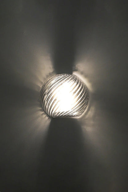 Silas Ribbed Glass Wall Sconce | Ribbed Glass, Metal | Close-up illuminated view against a dark charcoal backdrop, showing the dramatic starburst ribbed light patterns cast on the wall | vexa lamps