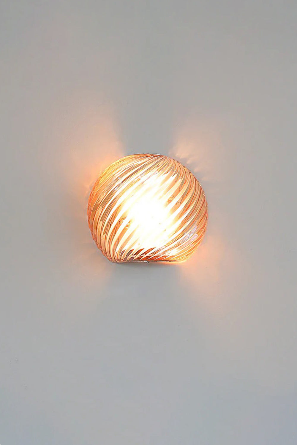 Silas Ribbed Glass Wall Sconce | Ribbed Glass, Metal | Staged illuminated view of the amber glass finish option radiating a rich orange-gold light halo on a light grey wall | vexa lamps