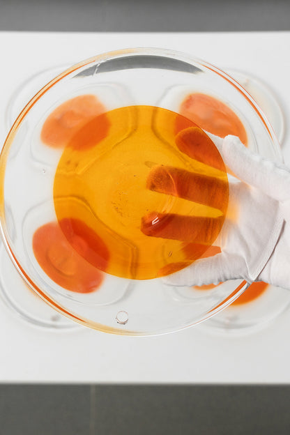 Close-up of a circular amber glass disc | Glass | Detail shot of a single disc being handled with a glove | vexa lamps