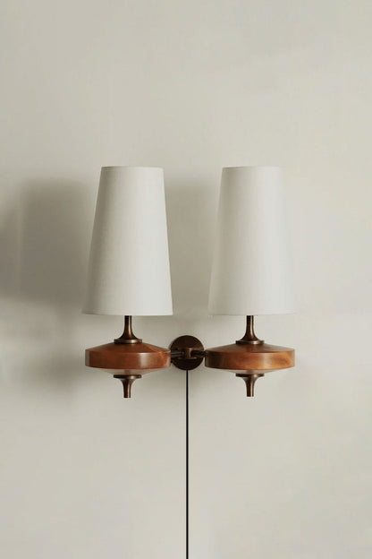 Spindle Walnut Wood Wall Sconce featuring a turned walnut-toned wood base and white fabric shades for warm accent lighting.