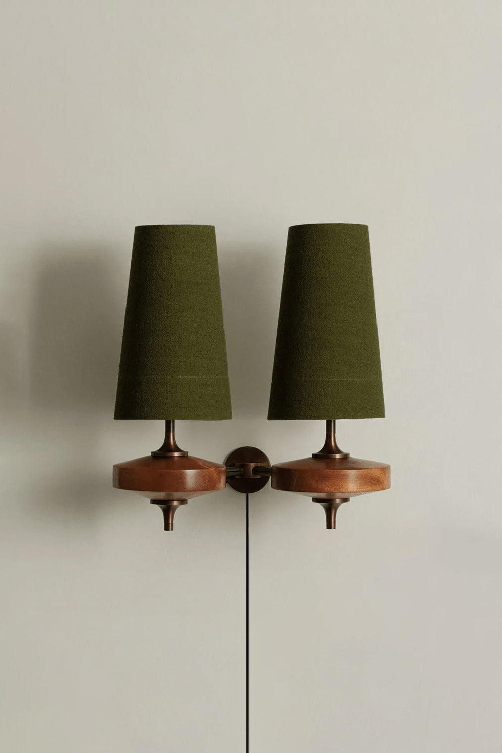 Spindle Walnut Wood Wall Sconce featuring green tapered fabric shades and a walnut base against a neutral wall.