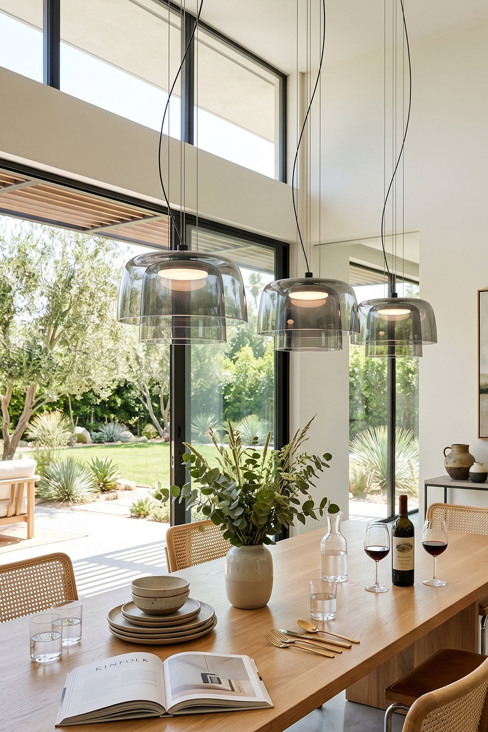 Stratum Layered Glass Pendant Light | Glass, Metal | A trio of smoky grey pendant lights lined up over a long wooden dining table facing a sunlit garden | vexa lamps