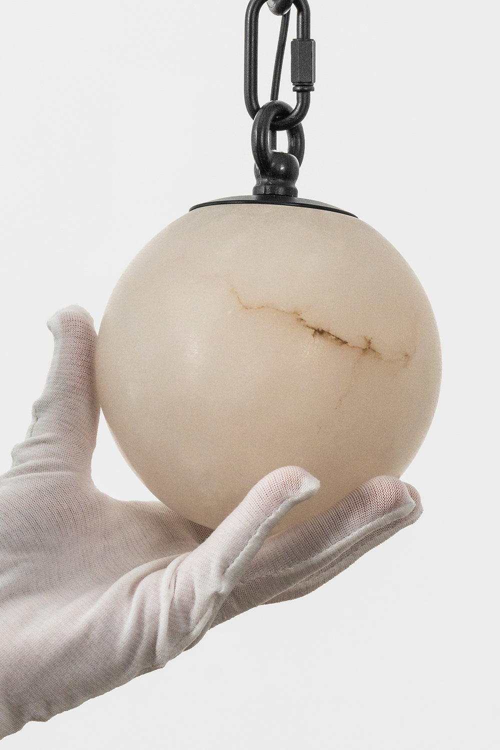 A hand holding a natural alabaster sphere from the Thalia Alabaster Spherical Chain Chandelier.