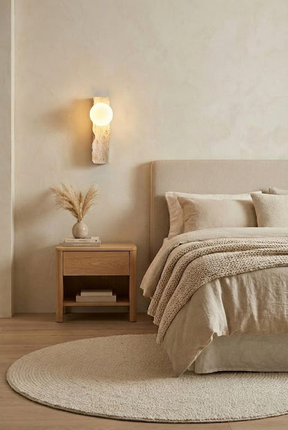 Bedside travertine wall light in a neutral bedroom | Yellow Travertine, Metal, Glass | Installed over a light wood nightstand and beige bedding | vexa lamps