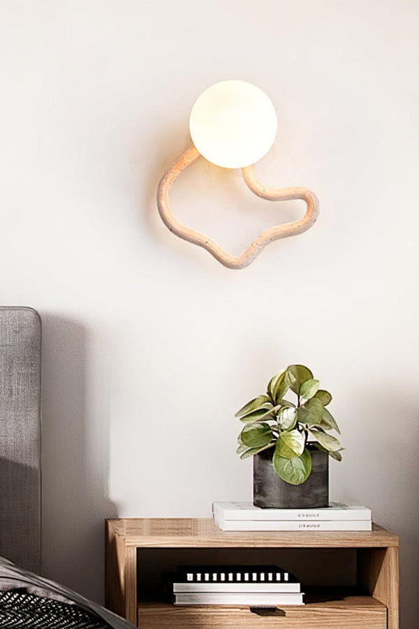 Modern travertine wall light with organic shape | Travertine, Glass, Wood | Mounted above a wooden nightstand with a small plant | vexa lamps