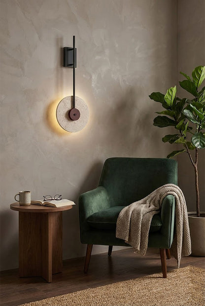 Modern travertine disc wall lamp providing backlighting | Travertine, Wood, Metal | Next to a green armchair in a minimalist lounge | vexa lamps