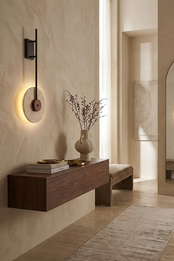 Lit travertine halo sconce on a beige wall | Travertine, Wood, Metal | Perspective view in a hallway over a wooden shelf | vexa lamps