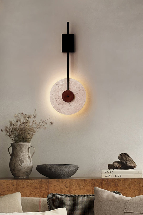 Travertine disk wall lamp above a decorative ledge | Travertine, Wood, Metal | Interior scene with ceramic vases and pillows | vexa lamps