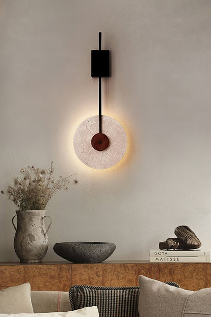 Travertine disk wall lamp above a decorative ledge | Travertine, Wood, Metal | Interior scene with ceramic vases and pillows | vexa lamps