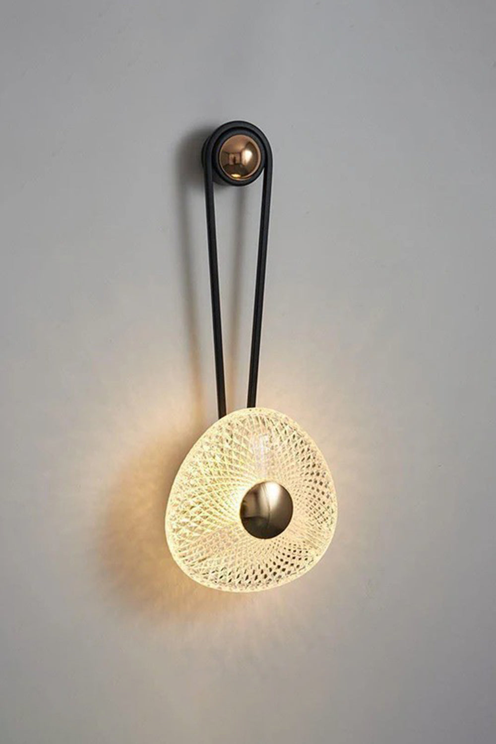Vara Aura Woven Acrylic Wall Lamp | Woven Acrylic, Brass | Fully illuminated wall sconce casting a warm, atmospheric glow against a neutral textured wall | vexa lamps