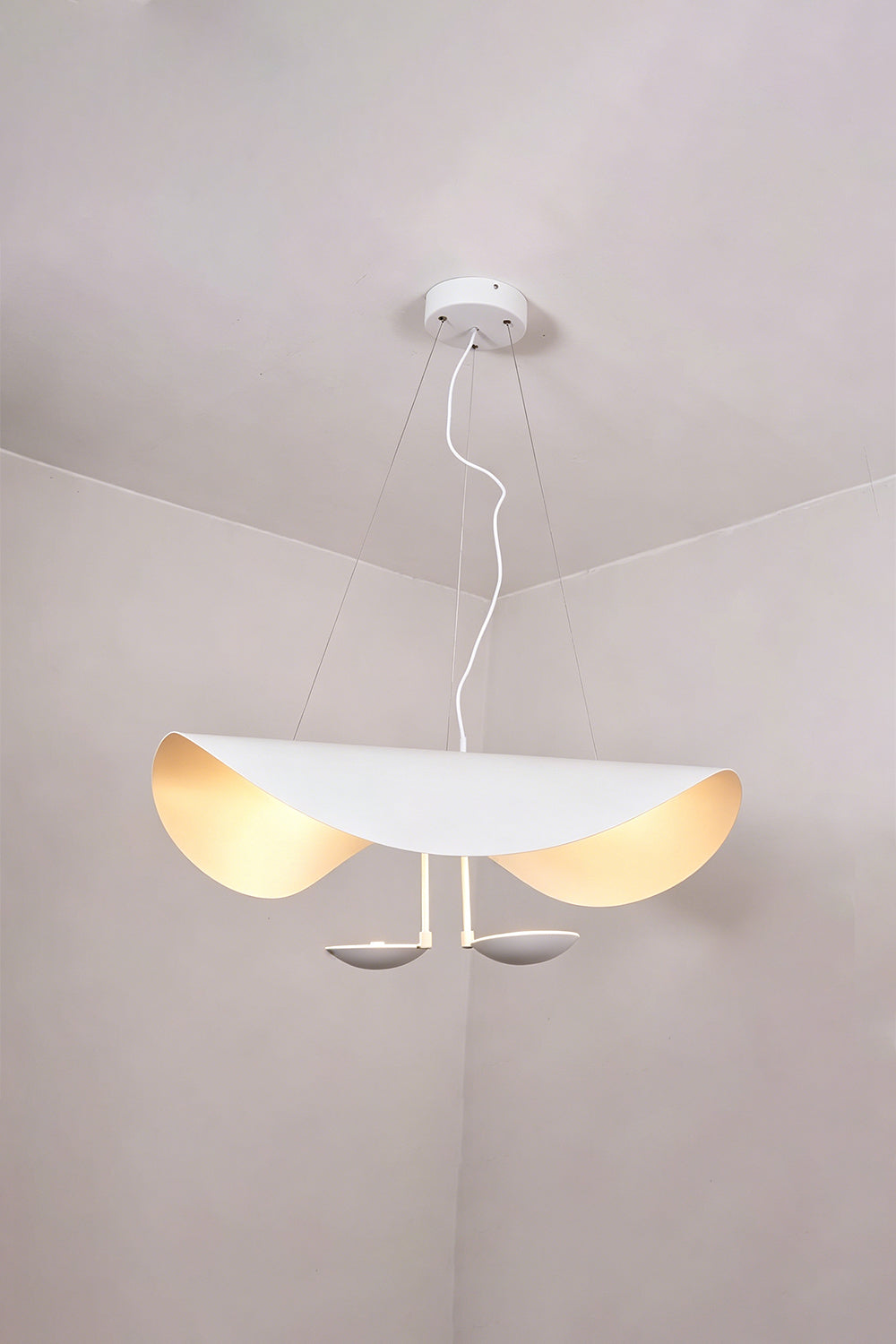 Voluta Horizon Metal Pendant Light | Metal | White variant hanging and glowing warmly in a minimalist room corner | vexa lamps